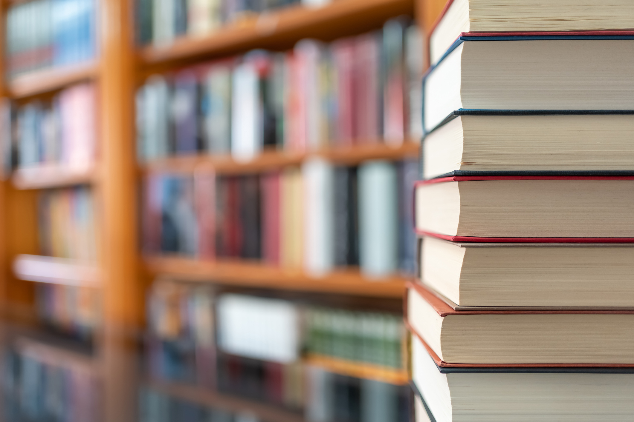 Stack of library books in front of library shelves full of books.