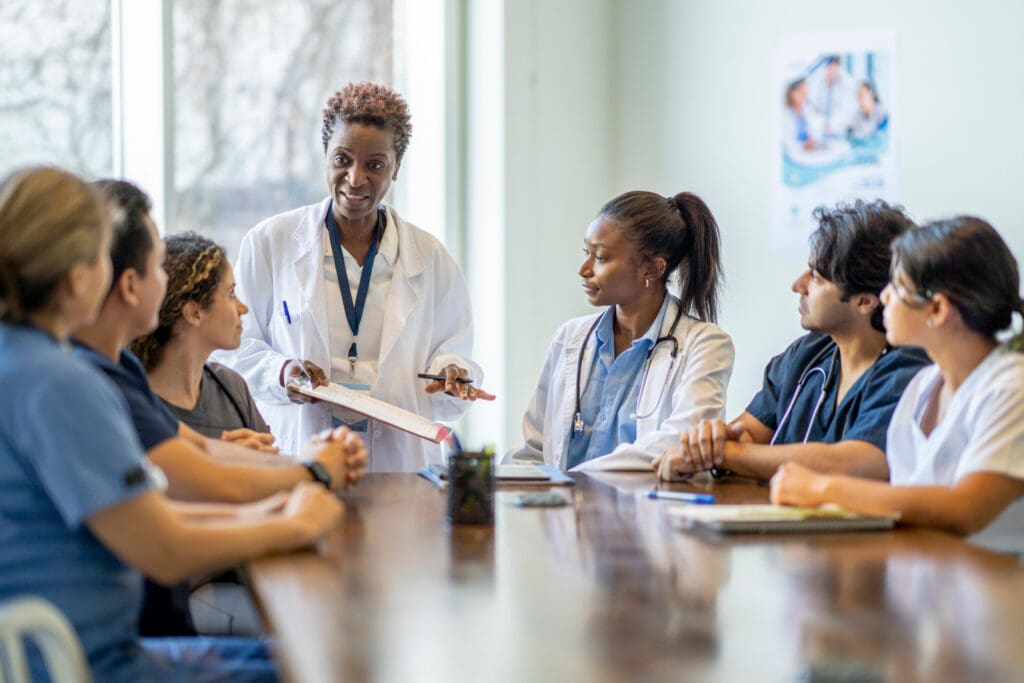 A group of students and a doctor discussing medical cases and treatments at a conference table.