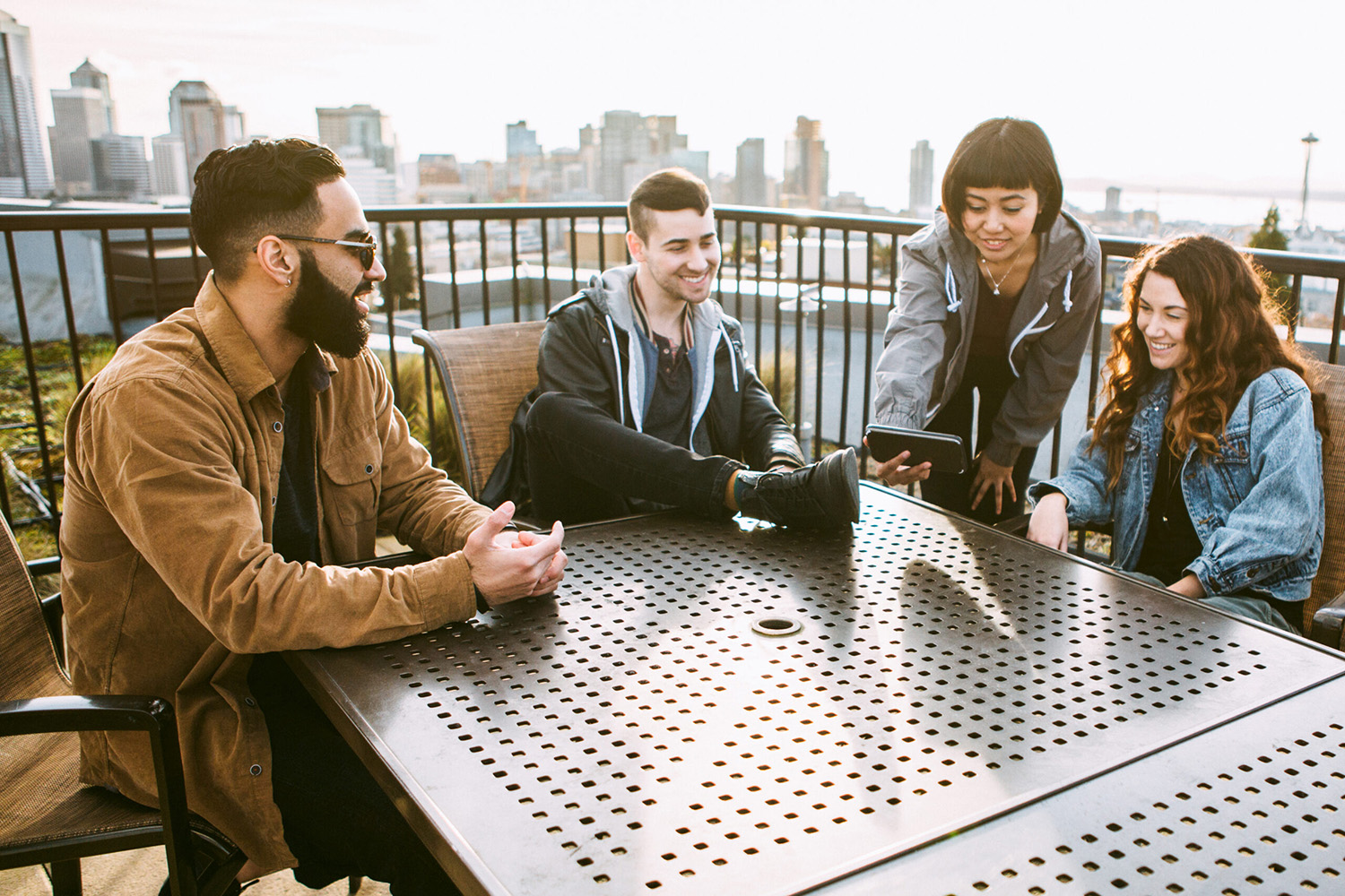 4 college aged young adults looking at a phone one is holding out as they sit at a table