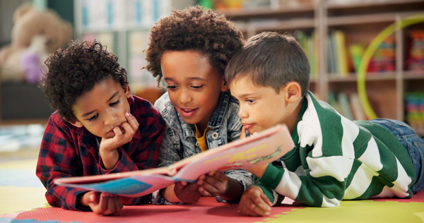 Three children reading a book on the floor of a library.