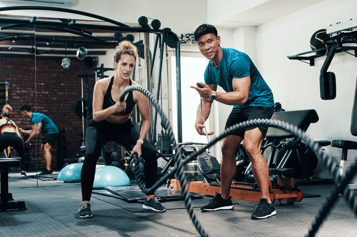 A man and woman engage in a workout session, using a rope for strength training and fitness exercises.